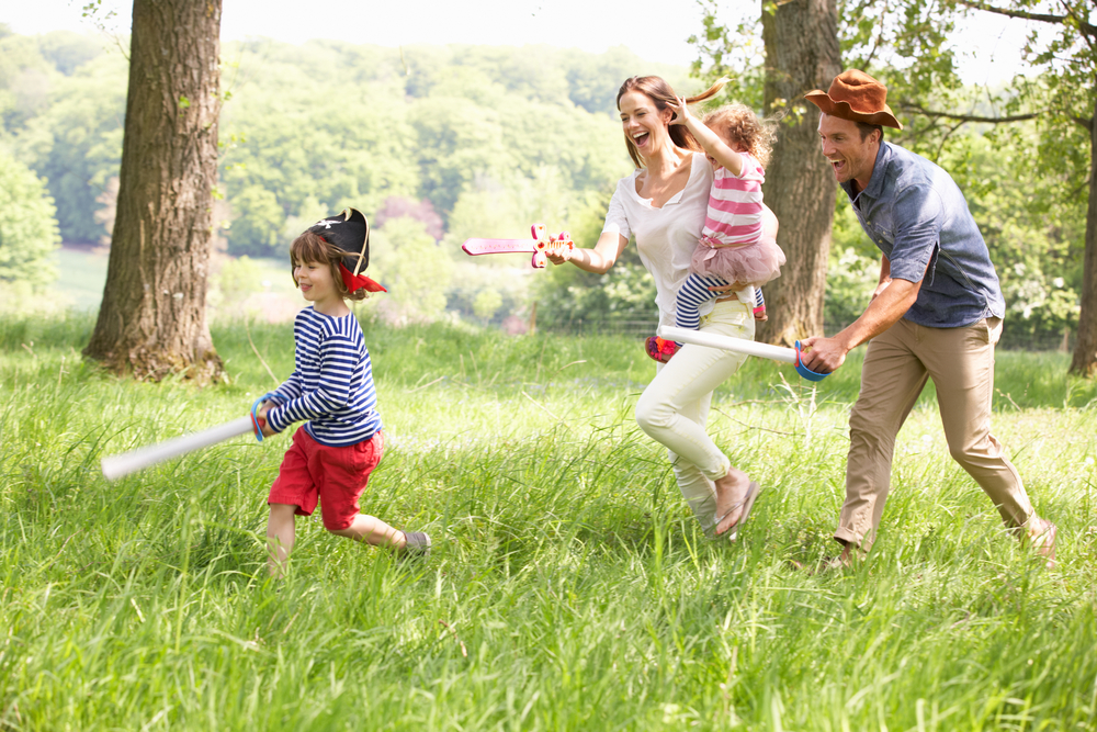 Parents Playing Exciting Adventure Game With Children In Summer Field