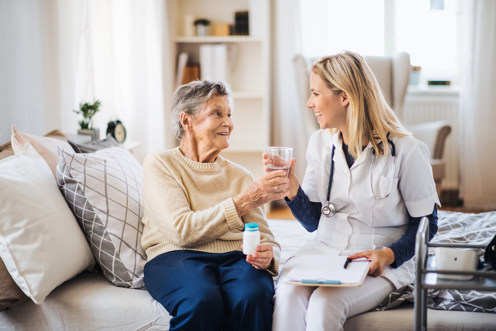 A health visitor giving a senior woman a glass of water to take pills.