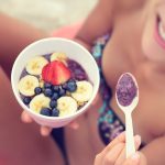 Acai bowl – girl eating healthy food on beach